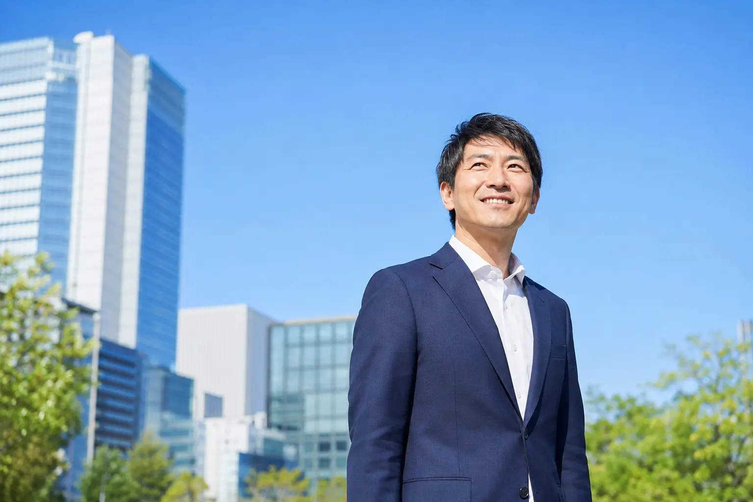 青空の都会で爽やかな笑顔を見せる40代の男性ビジネスマン
