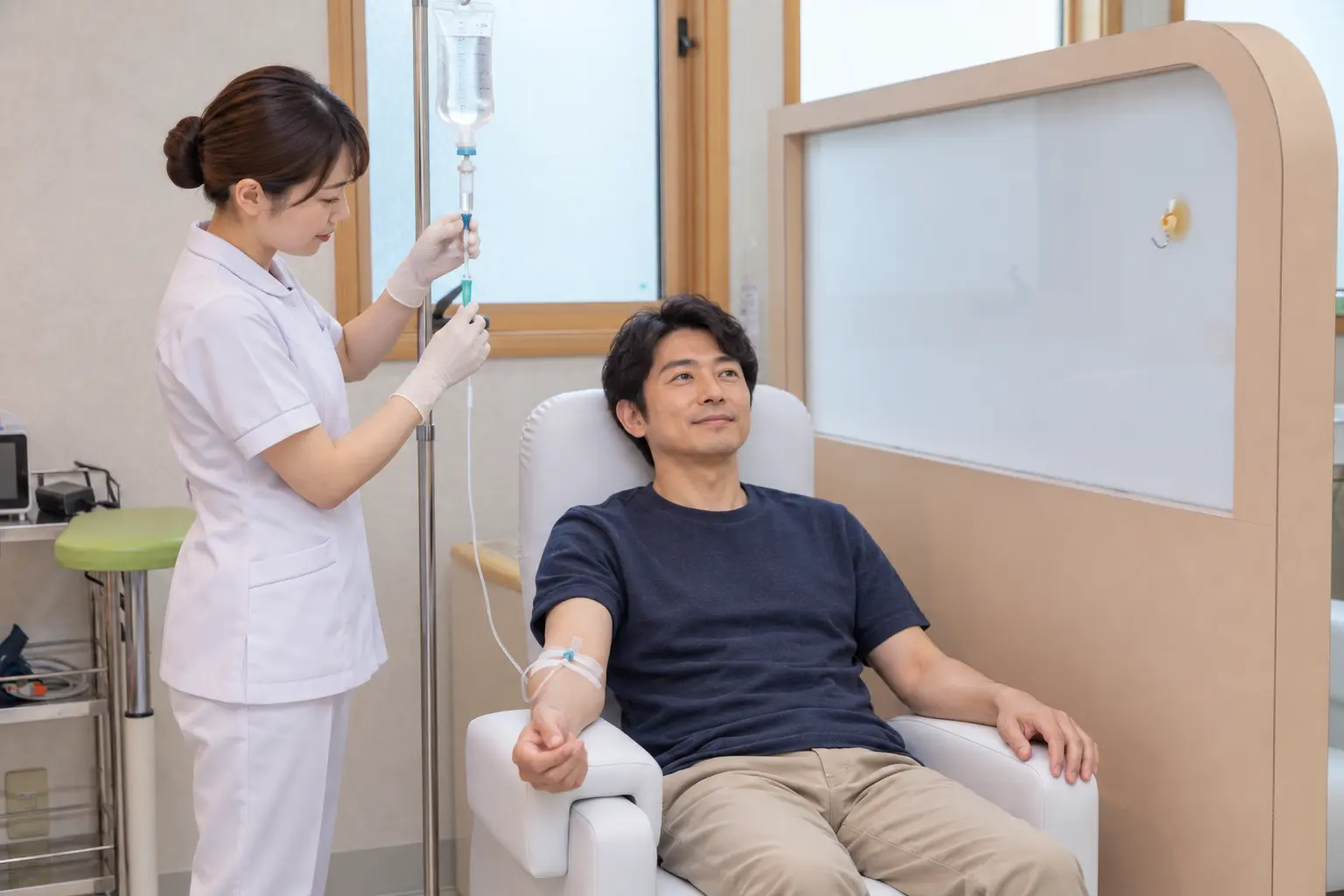 30代男性が点滴を受け、女性看護師が点滴を調整する様子